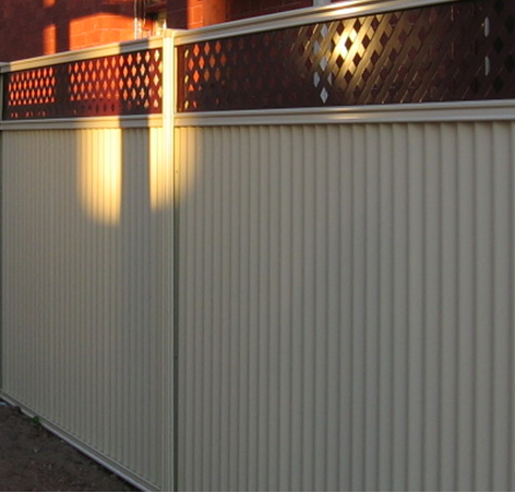 Cream-colored vertical slat fence with brown diamond lattice detail, casting shadows in sunlight.