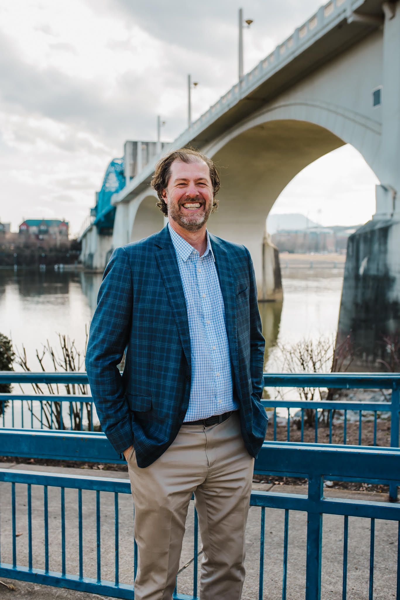 A man in a suit is standing on a bridge with his hands in his pockets.