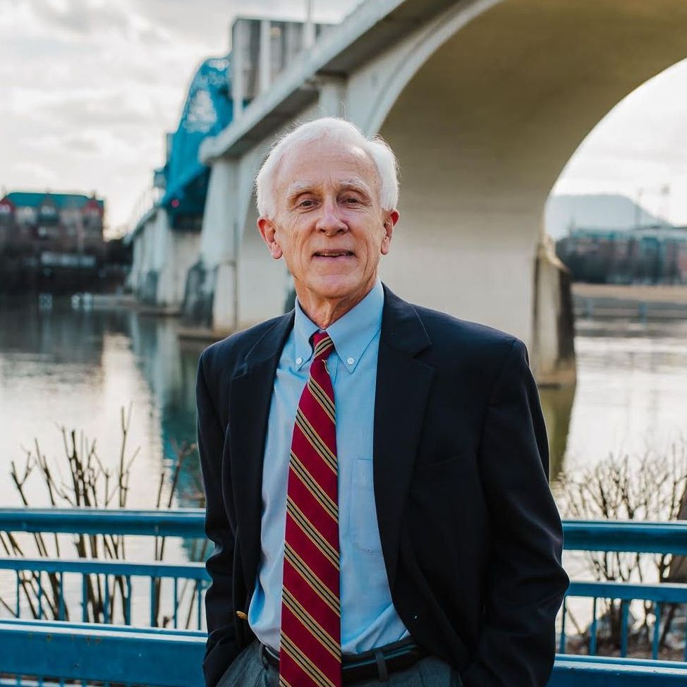 A man in a suit and tie is standing in front of a bridge.