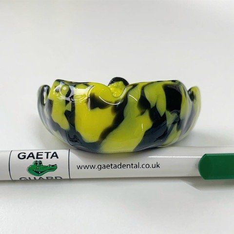 Yellow and black swirl mouthguard next to a pen with