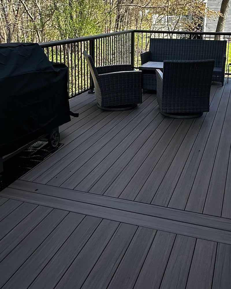 Deck with dark gray composite boards and black railing, outdoor furniture, grill covered in black.