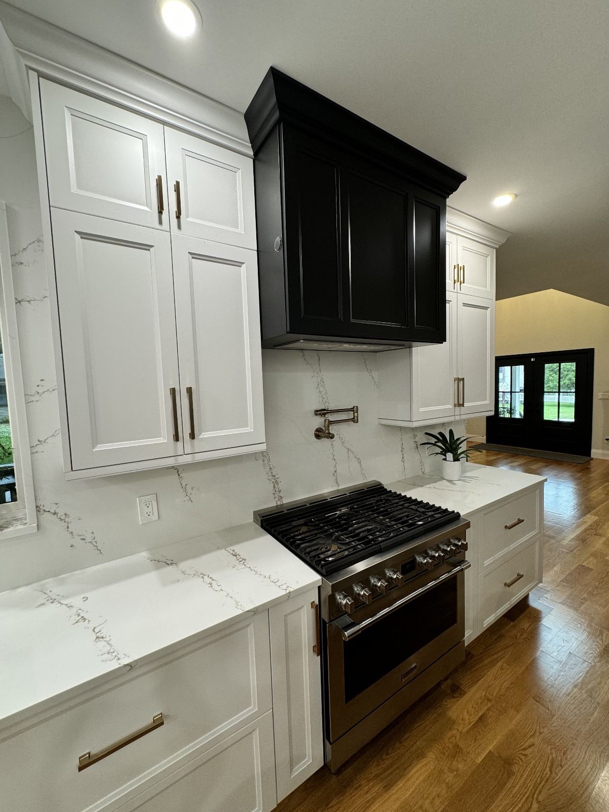 Modern white kitchen with black range hood and stainless steel appliances.