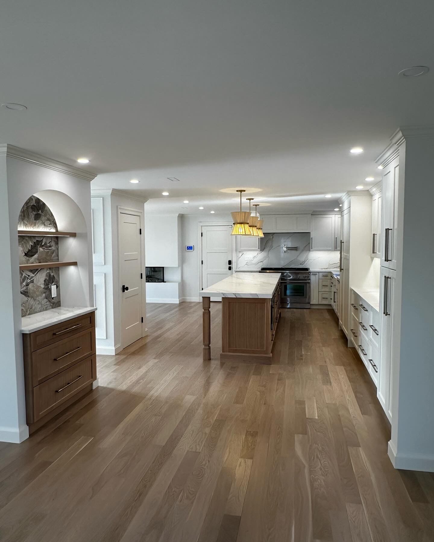 Spacious kitchen with wood floors, island, and white cabinets. Brown storage unit and wine rack on the left.