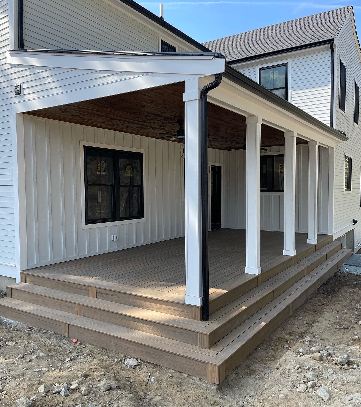 White house with porch and steps; brown decking and ceiling, black gutters, white pillars.