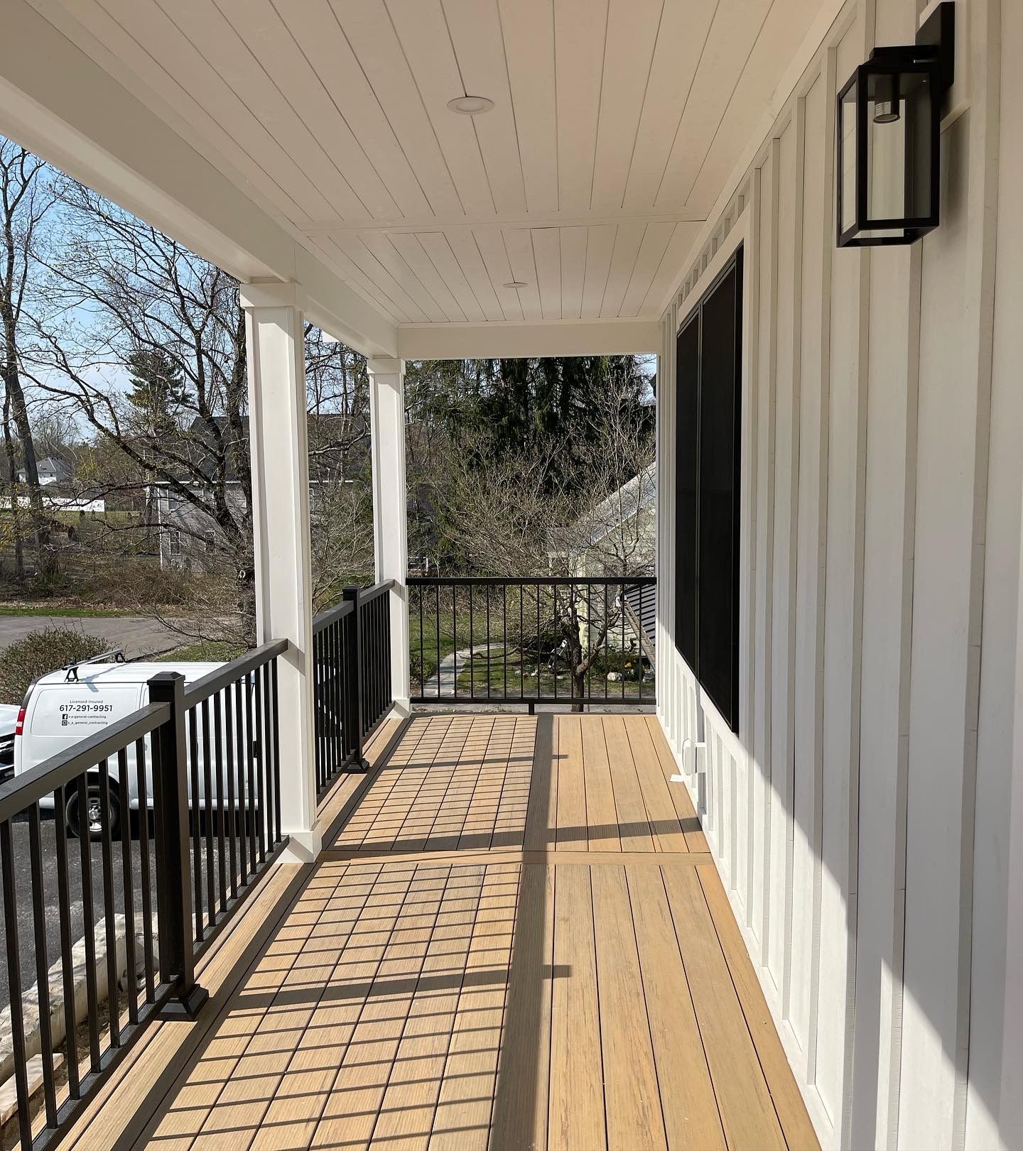 Covered porch with white panel siding, black railing and light fixtures, and wood floor.