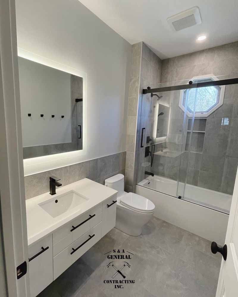 Modern bathroom with white vanity, toilet, and bathtub. Gray tiles on floor and wall. Black fixtures.