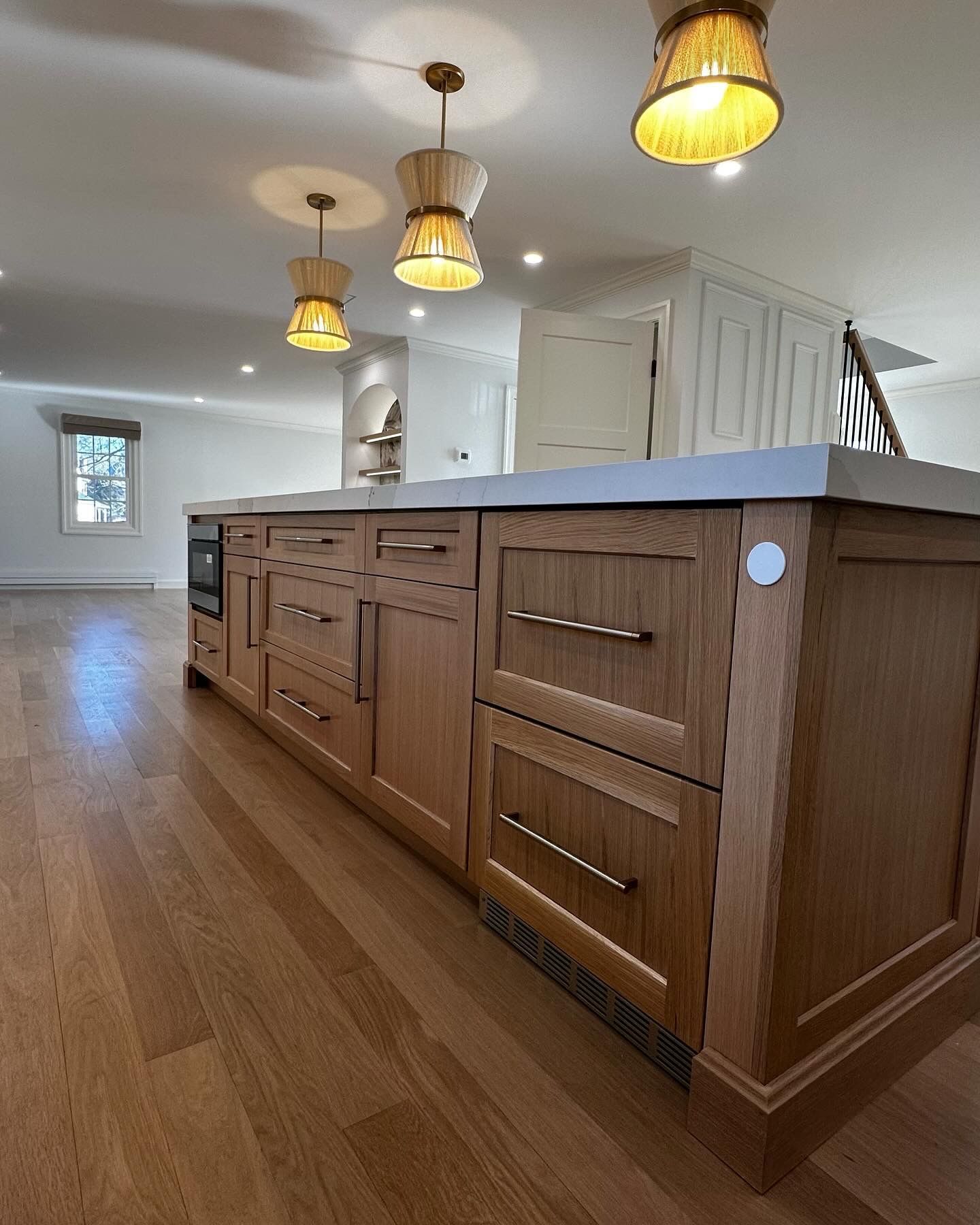 Wooden kitchen island with drawers, cabinets, and a concrete countertop, under pendant lights.
