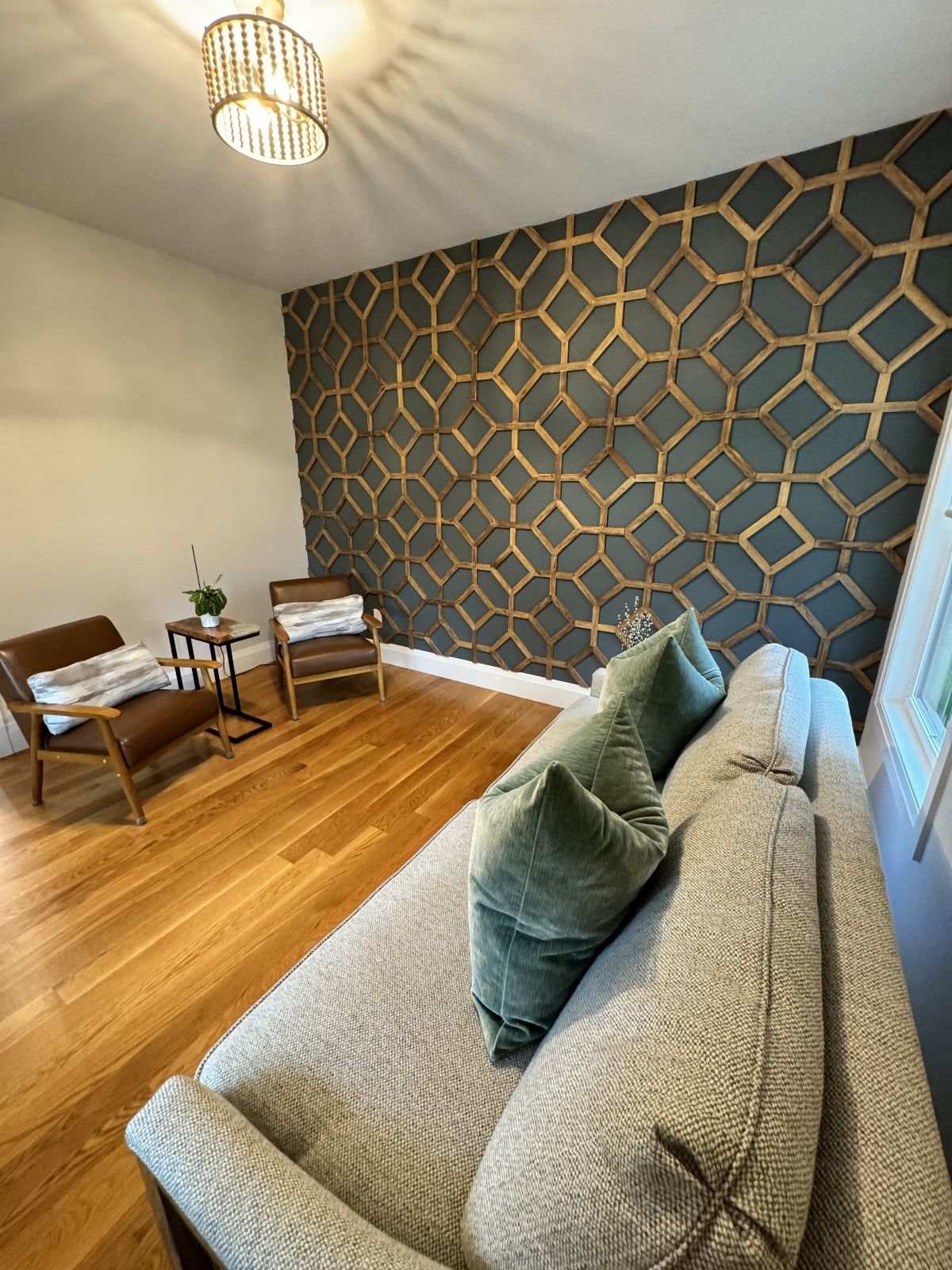 Living room with patterned accent wall, hardwood floor, sofa, chairs, and chandelier.