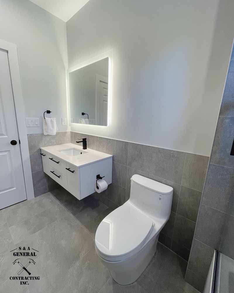 Modern bathroom with a white floating vanity, illuminated mirror, and a white toilet against gray tile.