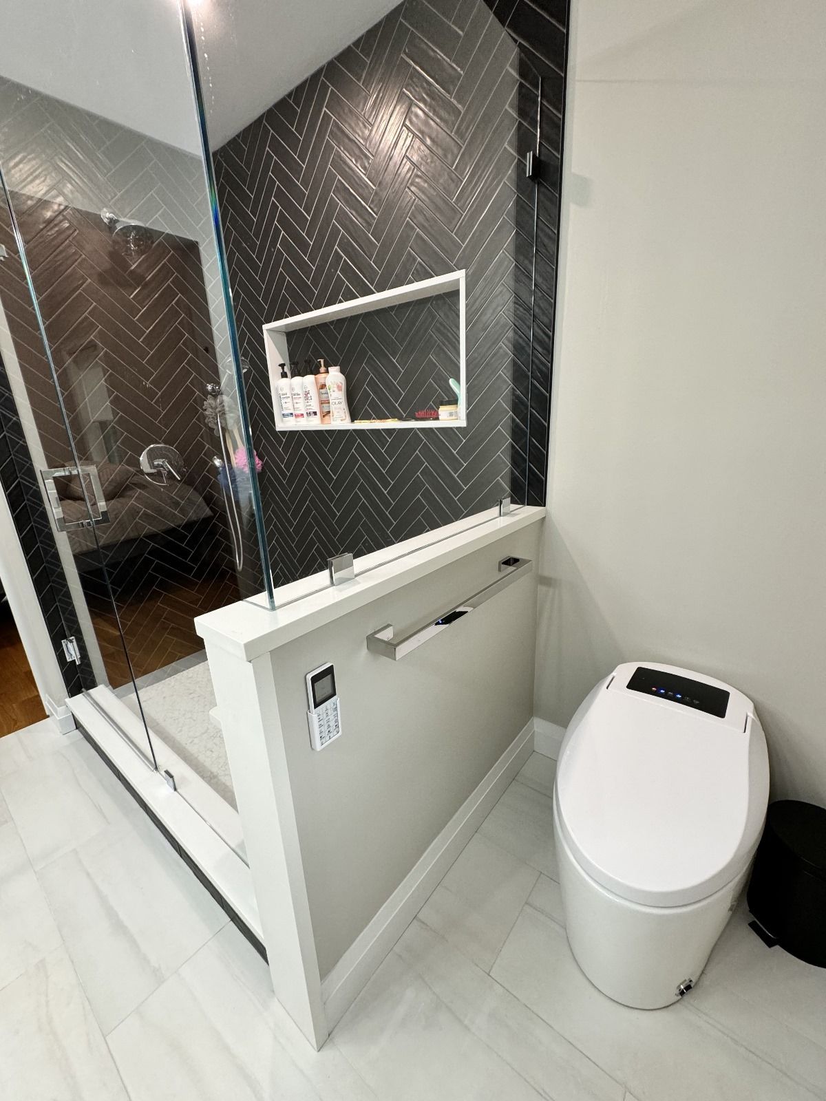 Modern bathroom with a walk-in shower, black herringbone tile, and a smart toilet.
