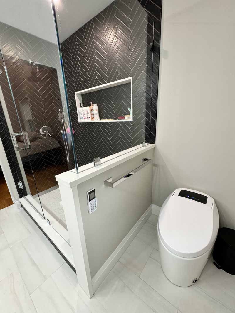 Modern bathroom with a white toilet, glass shower, and black herringbone tile wall.