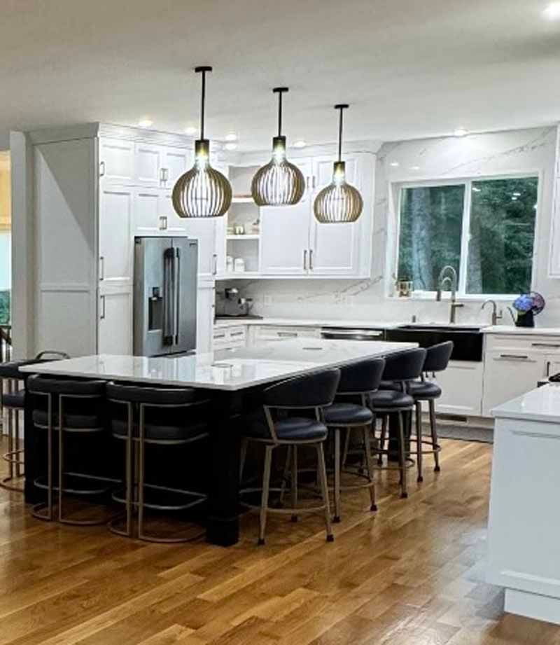 Modern kitchen with island, black stools, pendant lights, white cabinets, and stainless steel fridge.