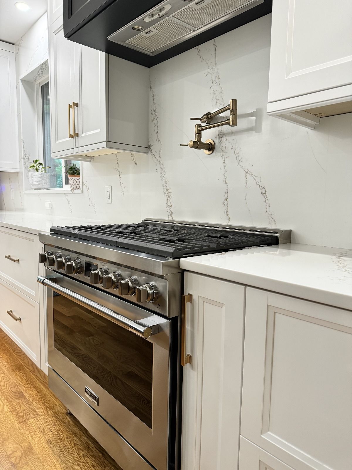 Stainless steel range and white cabinets in a kitchen, gold hardware, and a white backsplash with gray veining.