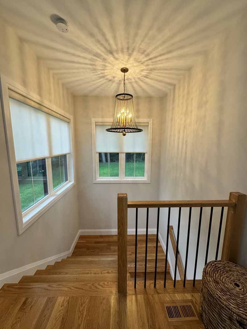 Stairwell with wooden steps, a chandelier, and windows with shades. Sunlight creates starburst pattern on ceiling.