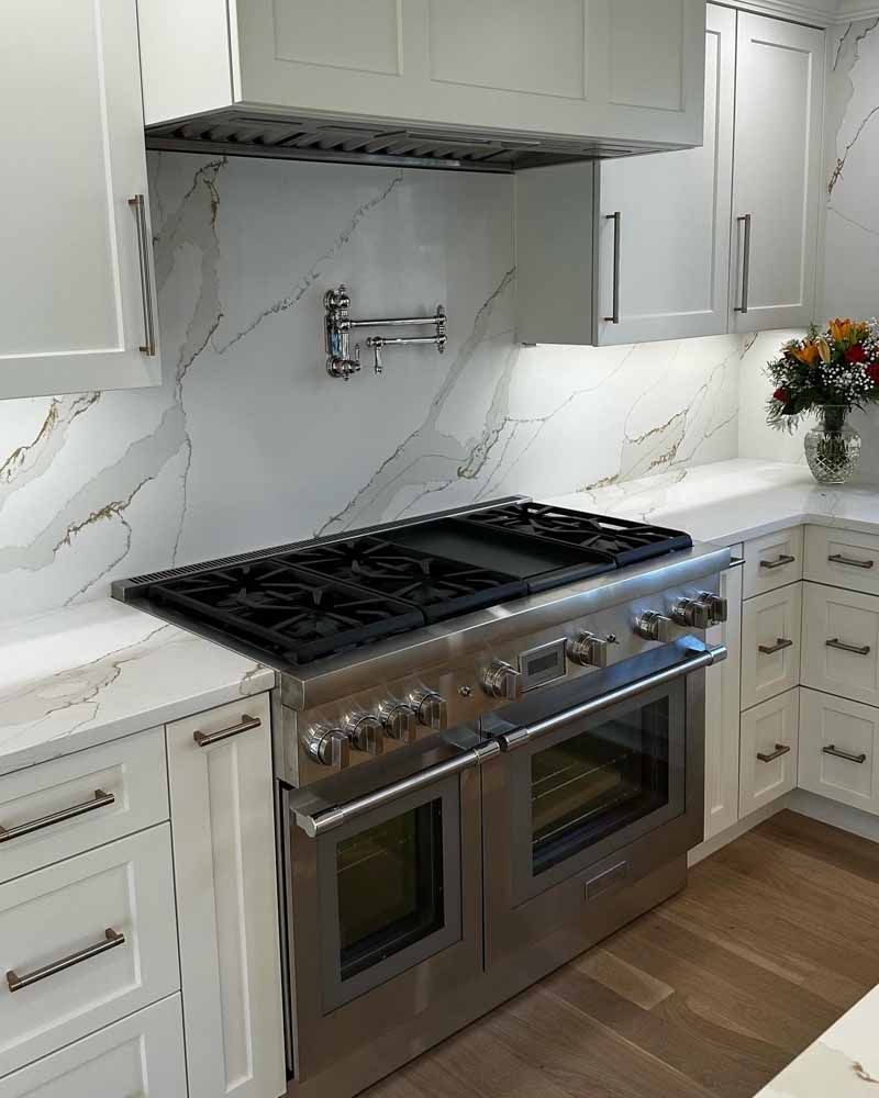 Stainless steel range and white cabinets in a kitchen with marble backsplash and hardwood floors.