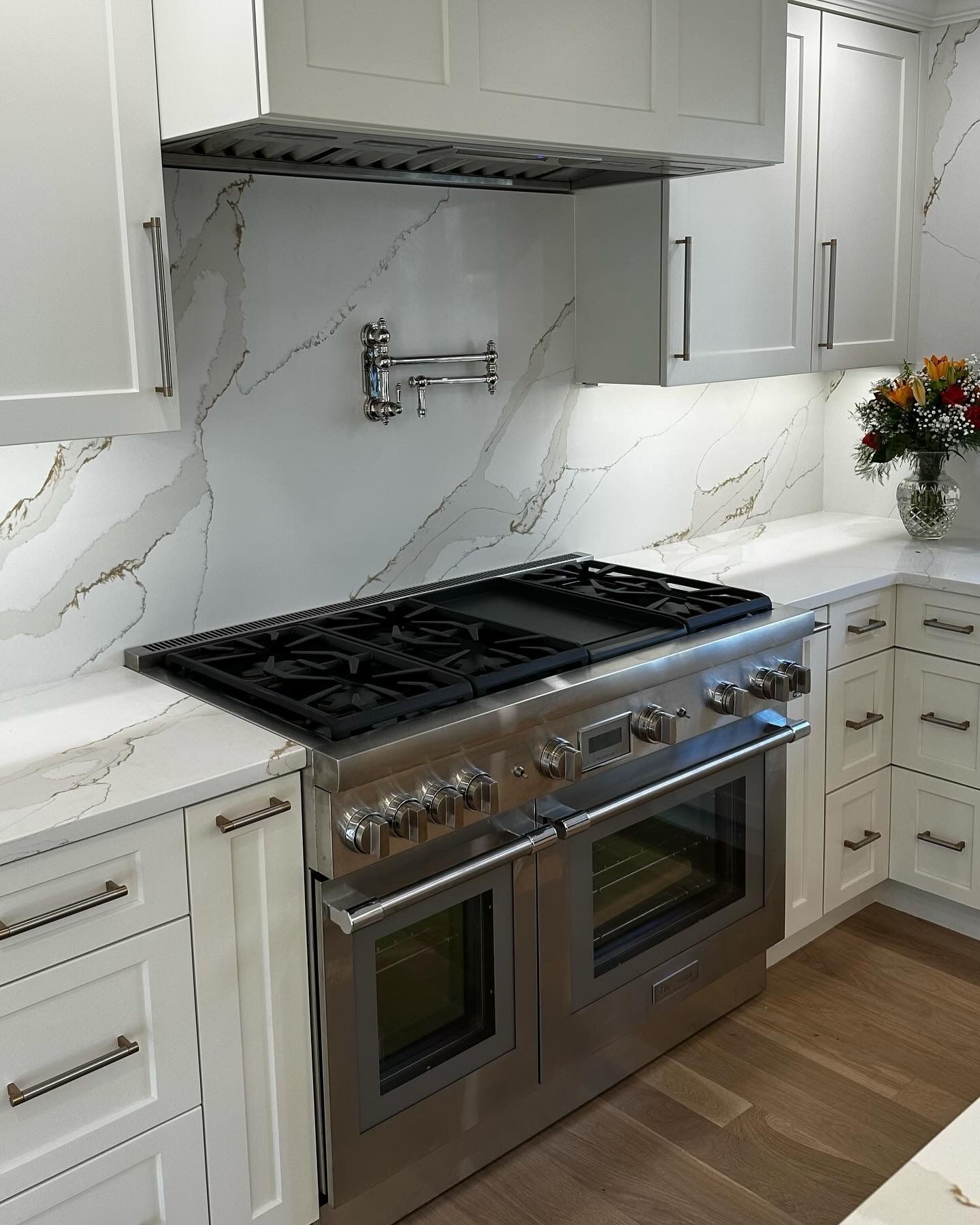 Stainless steel range in a white kitchen with marble backsplash and cabinets.