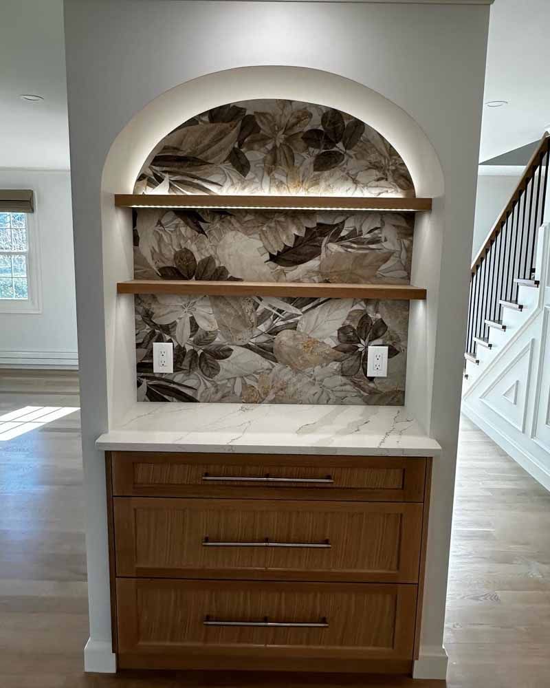 Built-in wooden cabinet with an arched alcove and shelves.  Floral backsplash and recessed lighting.
