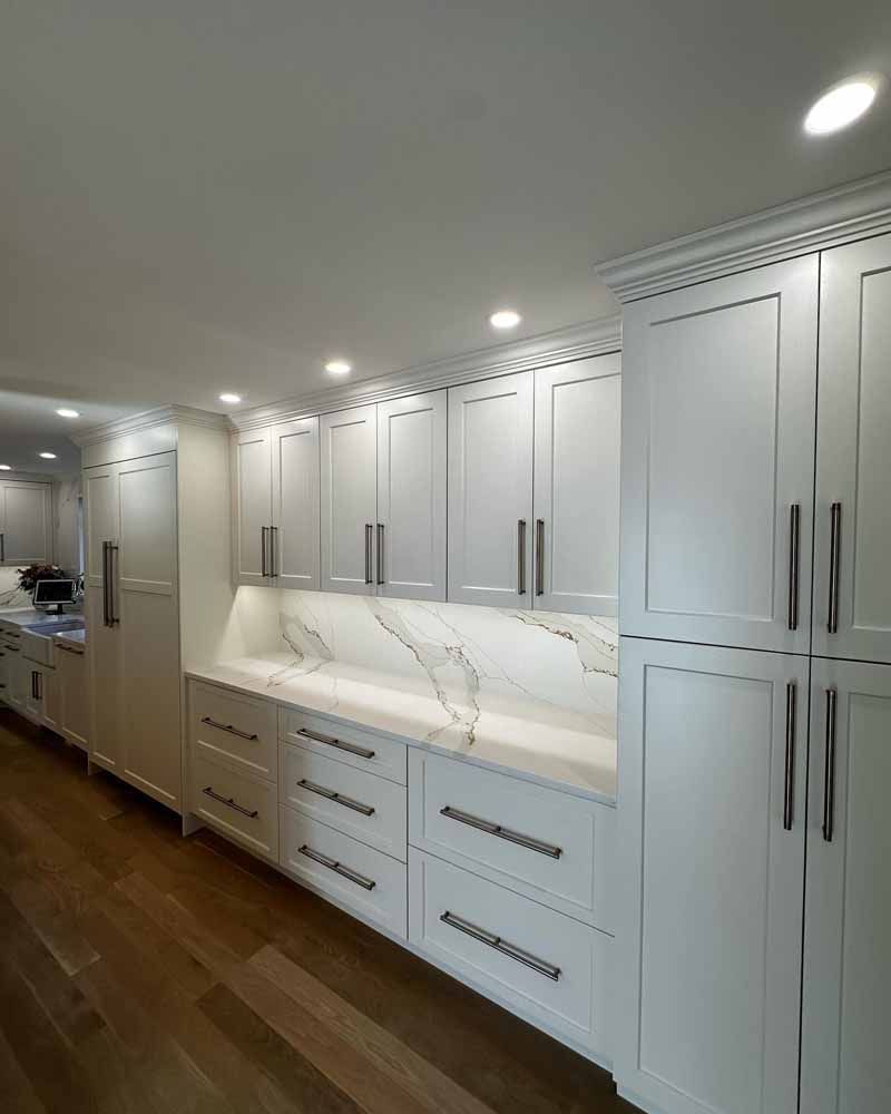 White kitchen cabinets with marble backsplash and stainless steel hardware.