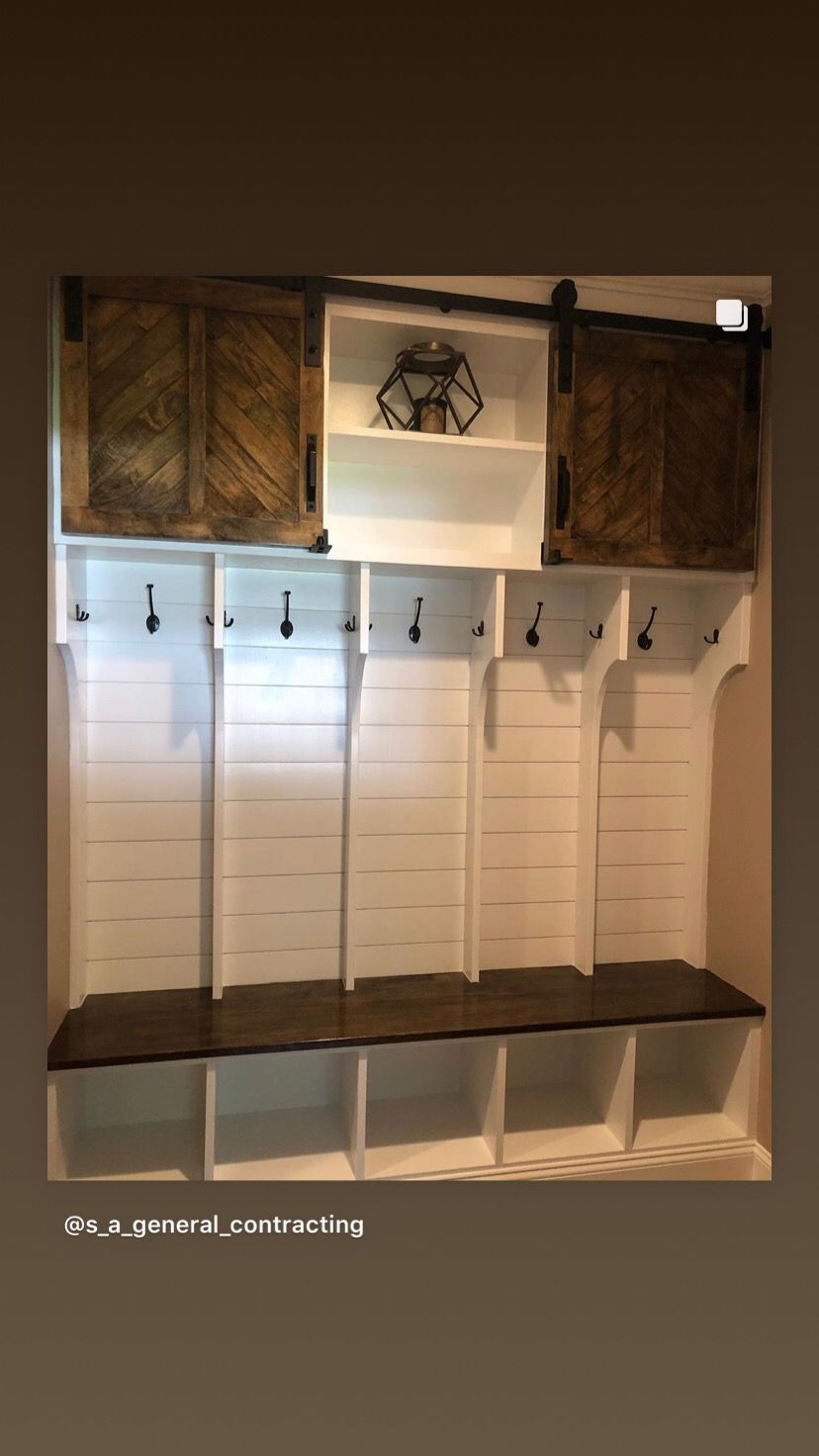 White built-in entryway storage unit with cubbies, a bench, coat hooks, and sliding barn doors with shelf.