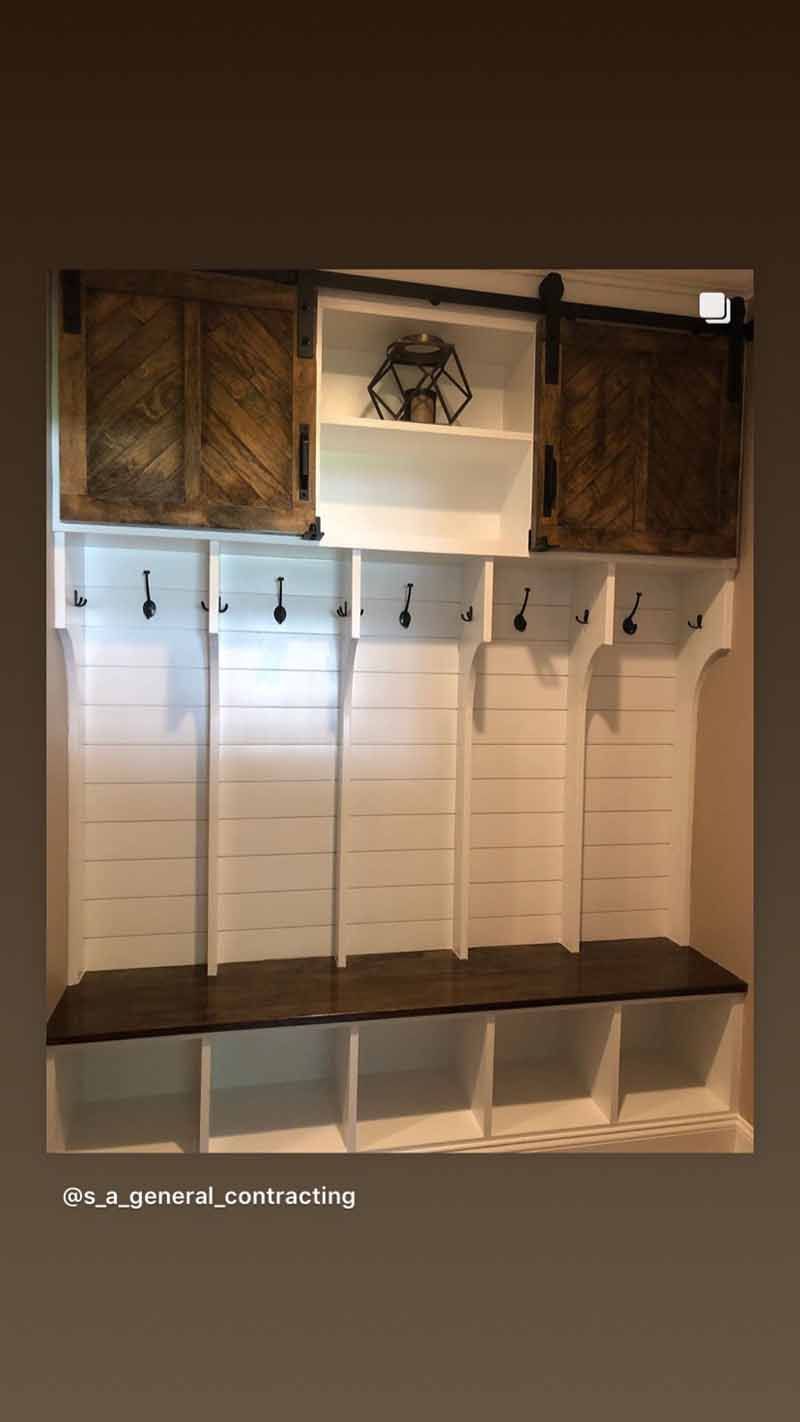White storage unit with dark wood bench, coat hooks, and sliding barn doors.
