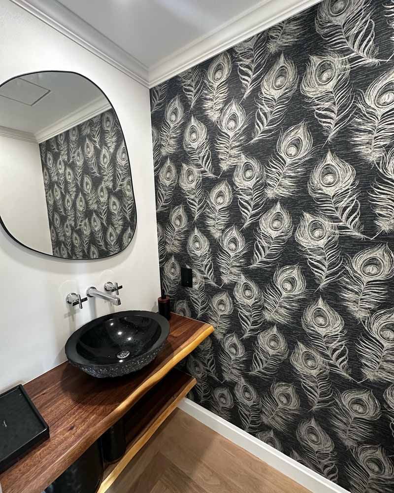 Bathroom with peacock feather wallpaper, black sink on a wooden counter, and an oval mirror.