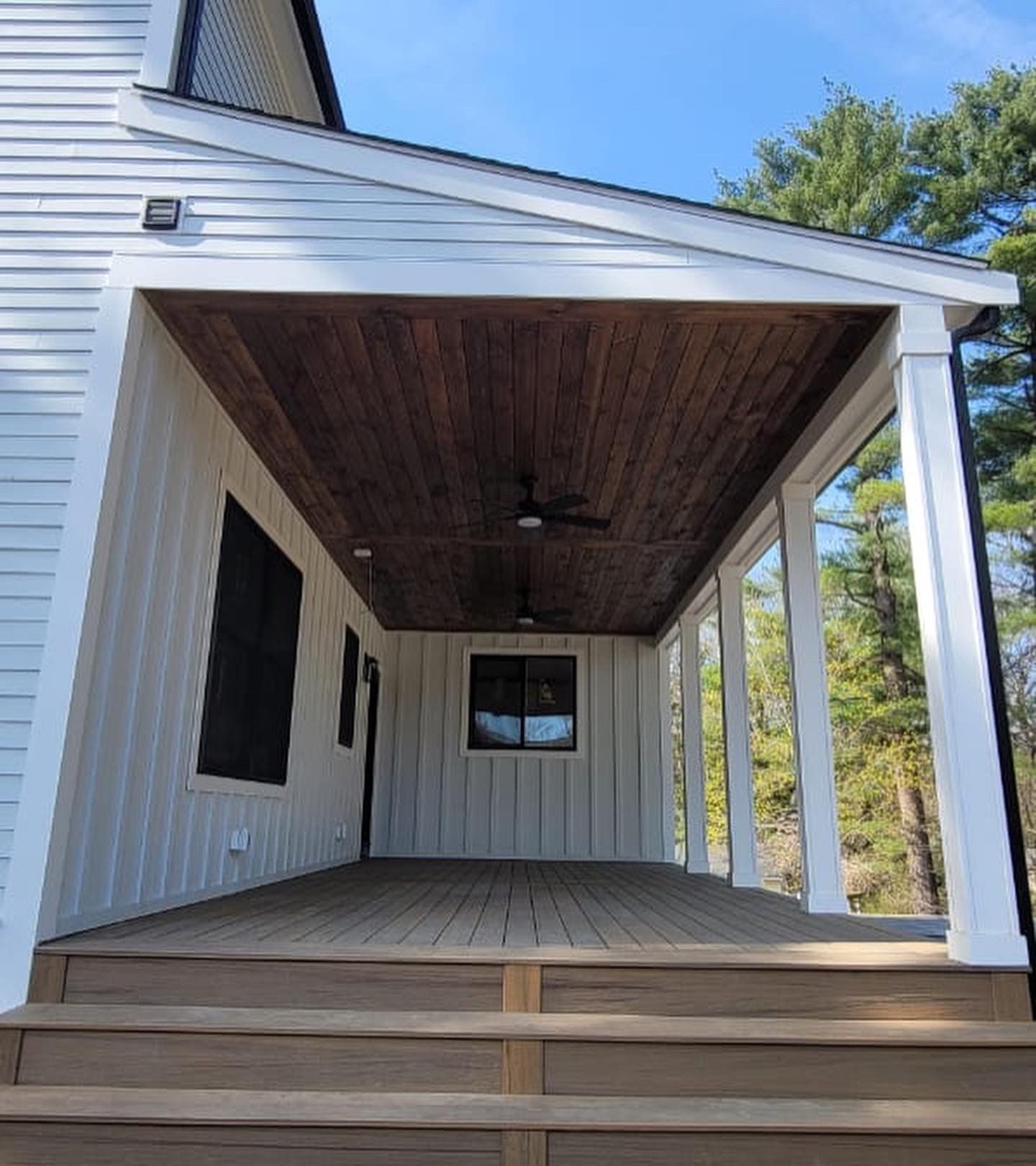 Covered porch with white siding, wood ceiling, composite deck, and black windows.