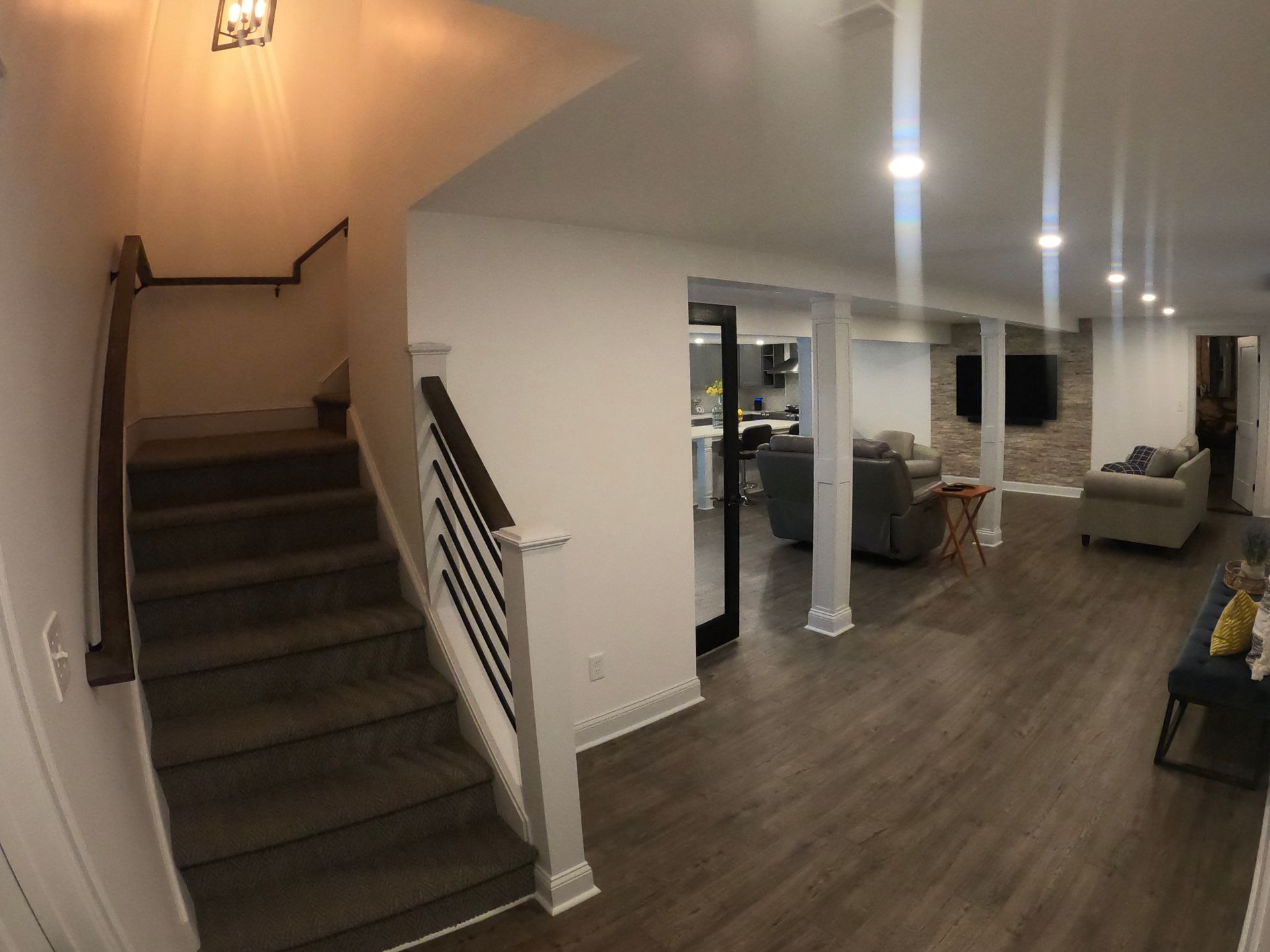 Basement with stairs, wood floors, and white walls. A seating area with a TV is visible.