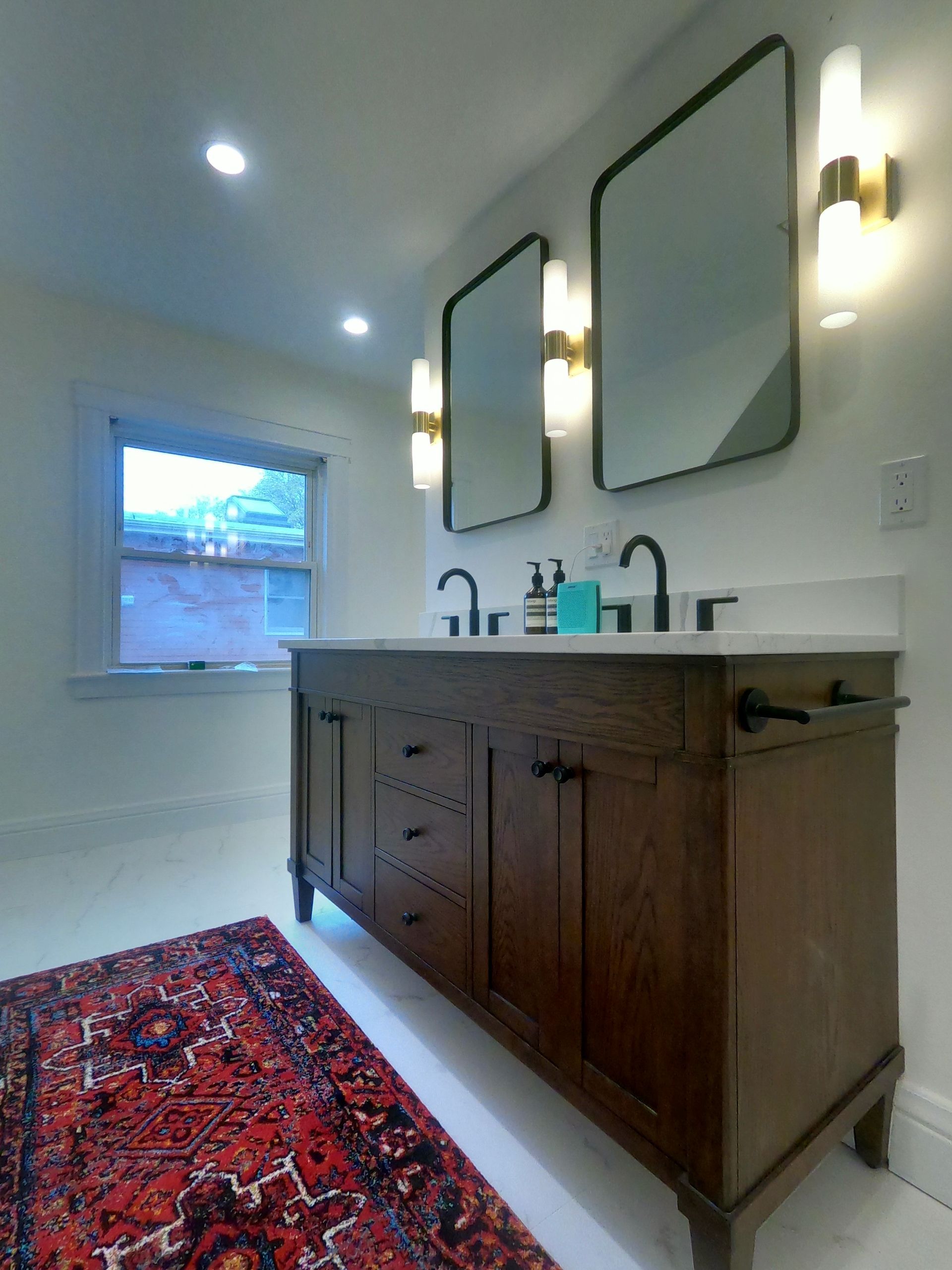 Bathroom with a wooden vanity, two mirrors, and a red rug.