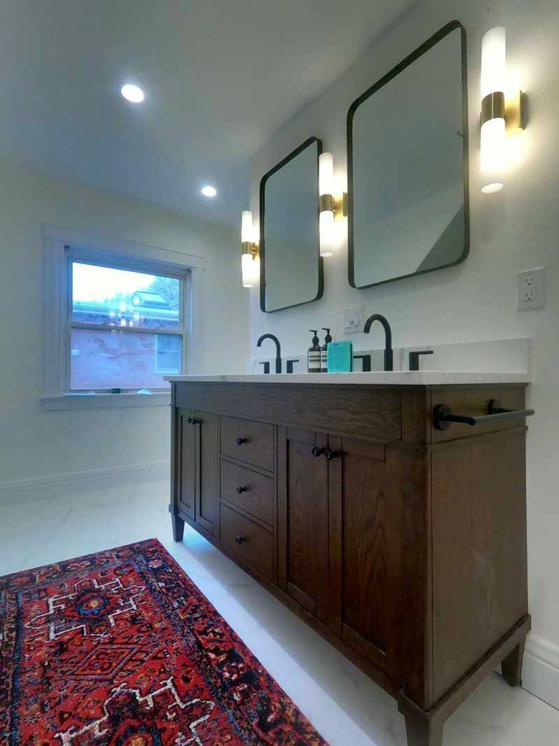 Bathroom with a dark wood vanity, two mirrors, and a red rug.