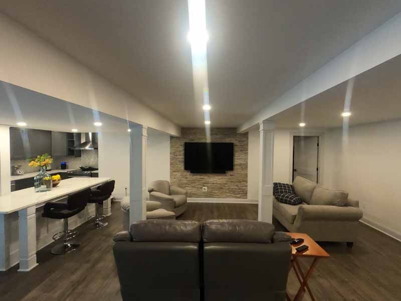 Modern living room with kitchen, seating area, and TV. Neutral colors, recessed lighting, and stone accent wall.