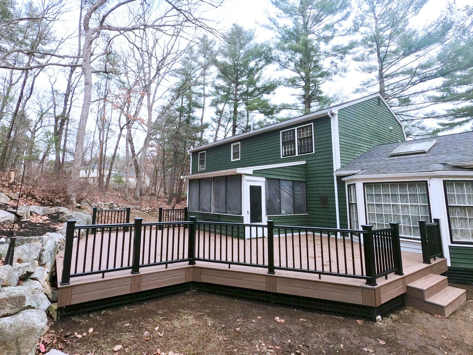 A two-level deck with black railings and composite decking, attached to a green house, surrounded by trees.