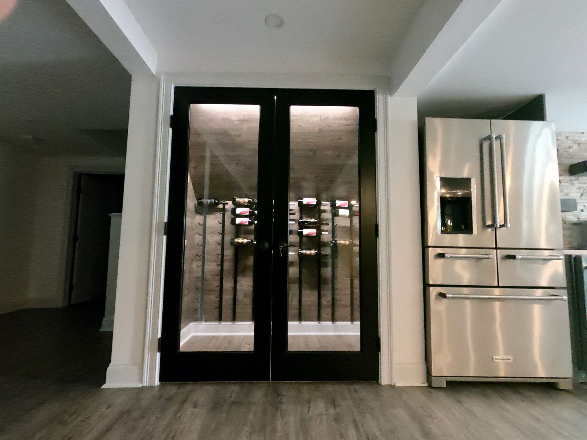 Black-framed glass doors lead to a wine cellar, next to a stainless steel refrigerator.