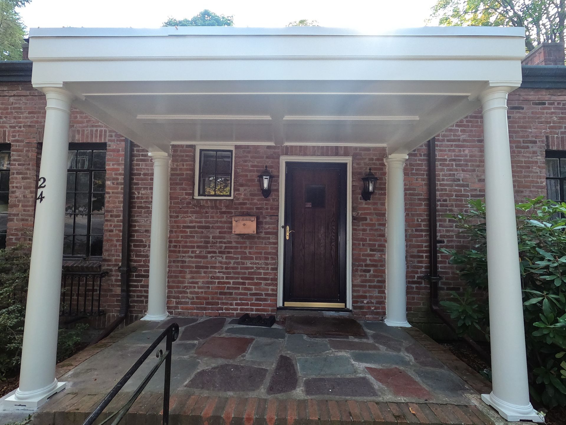Brick building with white-columned entrance and dark door. Porch with stone floor and black handrail.