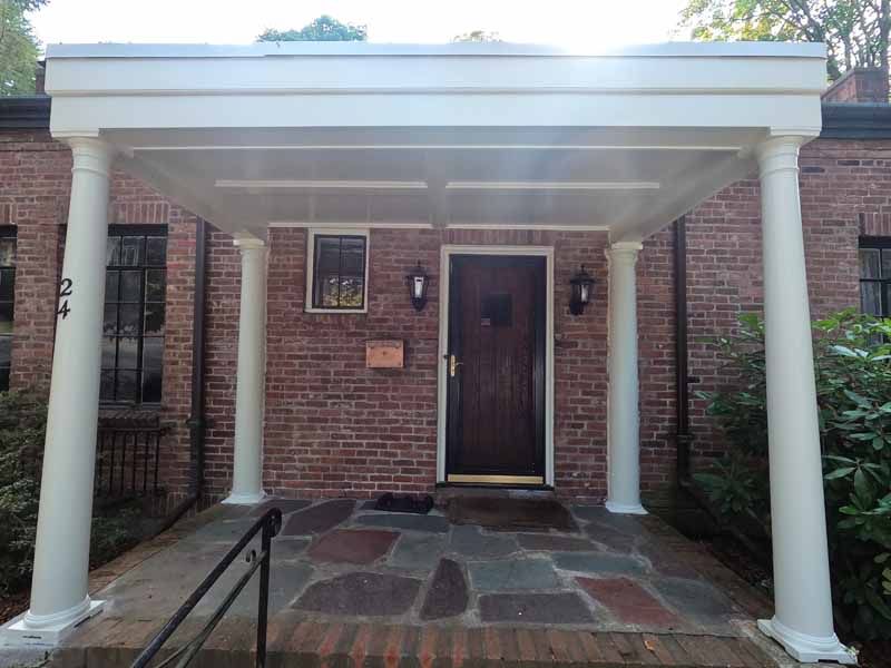 White-columned portico over a brick building's entrance; slate pathway, door with sconces.