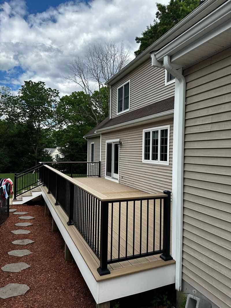 Deck with black railing next to a two-story house with beige siding and white gutters.