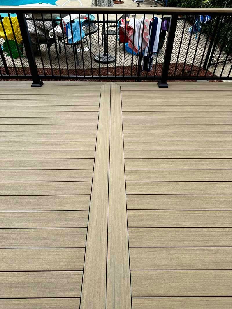 View of a wooden deck with warped center boards. Black railing with laundry hanging in the background.