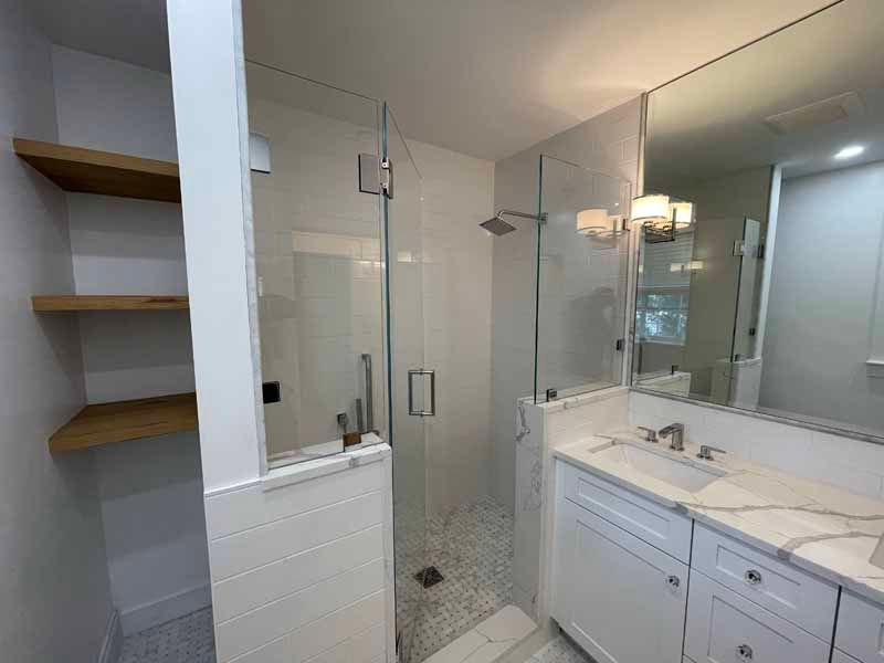 Bathroom with glass shower, white vanity, marble countertop, and wooden shelves.