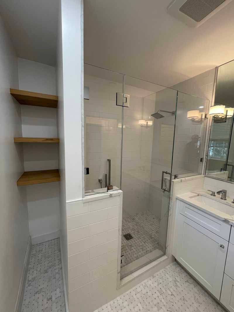 Modern white bathroom with shower and shelves. White tile, wood shelves, glass shower door.