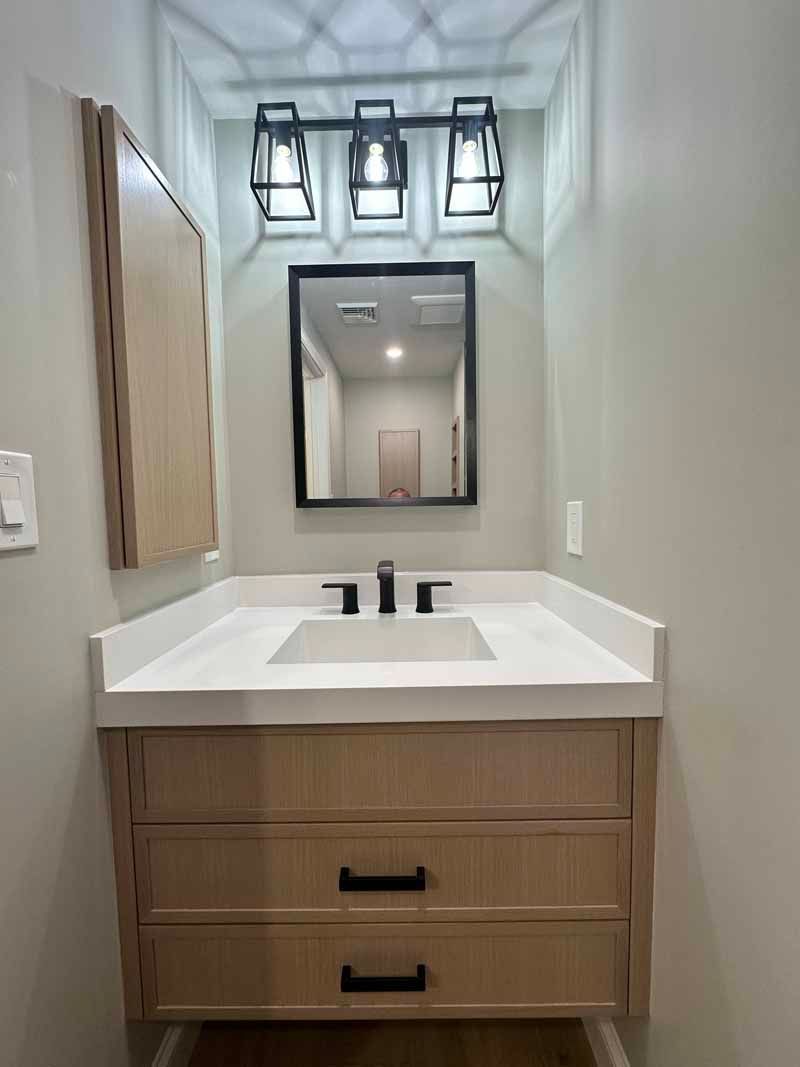 Bathroom vanity with wood-tone cabinet, quartz countertop, black faucet, mirror, and geometric light fixture.
