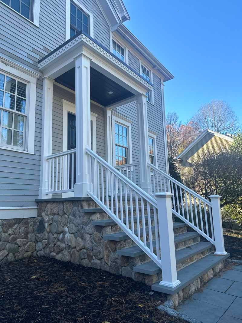 Gray house with stone steps and white railing leading to a covered porch.