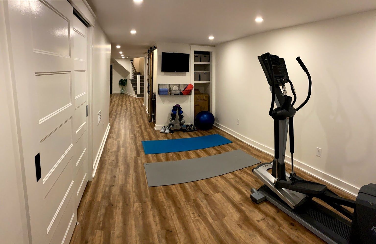 Home gym with elliptical machine, yoga mats, and storage.