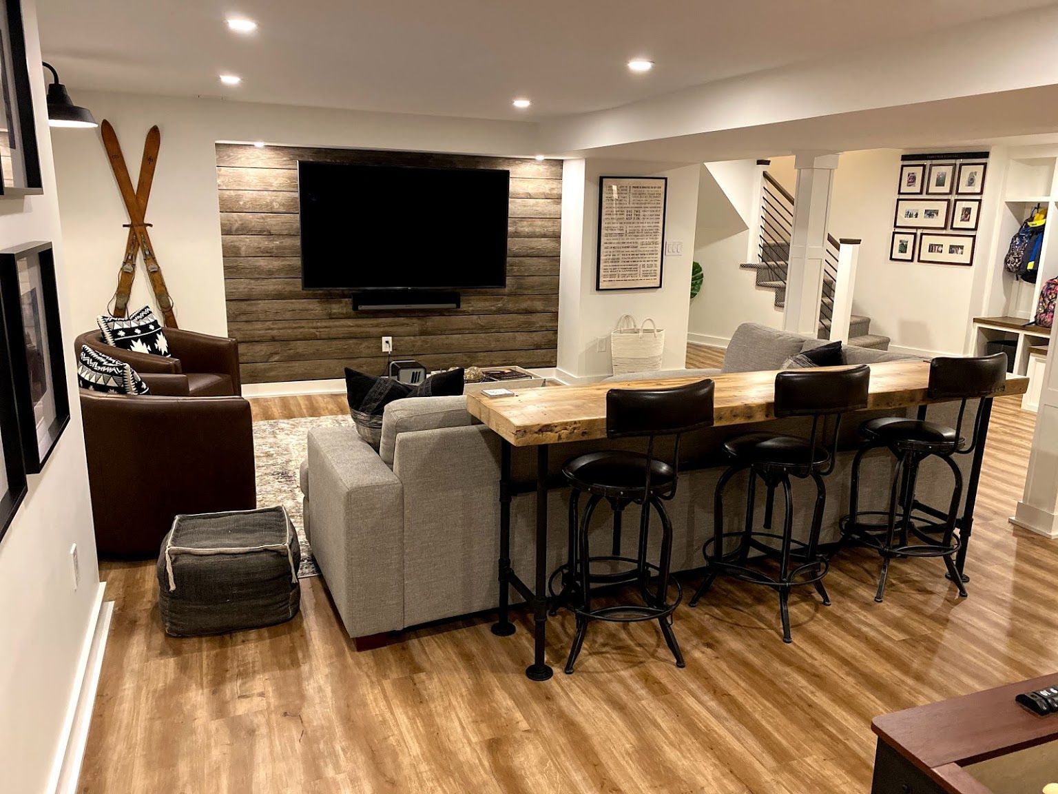 Cozy basement living area with large TV, sectional couch, bar seating, and wood accent wall.