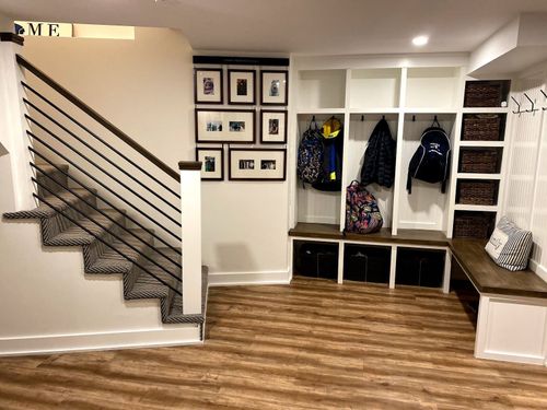 Entryway with stairs, built-in storage lockers, bench, and decorative framed photos on a white wall.