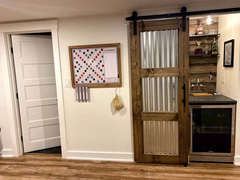 Basement room with a sliding barn door covering a small bar area. Scrabble board on the wall.