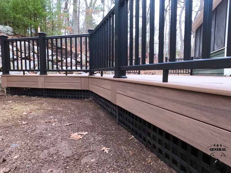 Brown and black deck with lattice skirting and black railing in an outdoor setting.