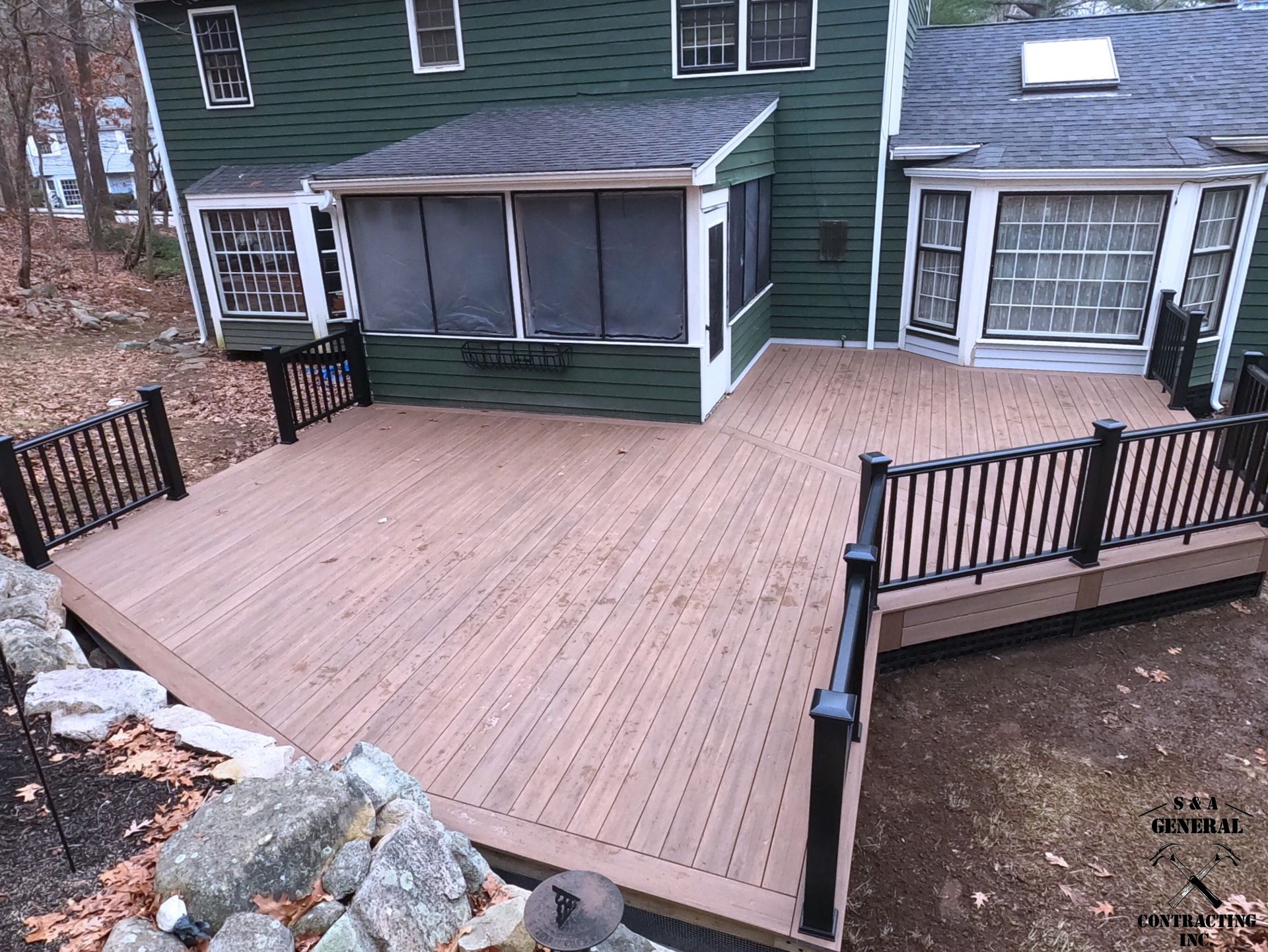A composite deck with black railing and screened-in porch attached to a green house.