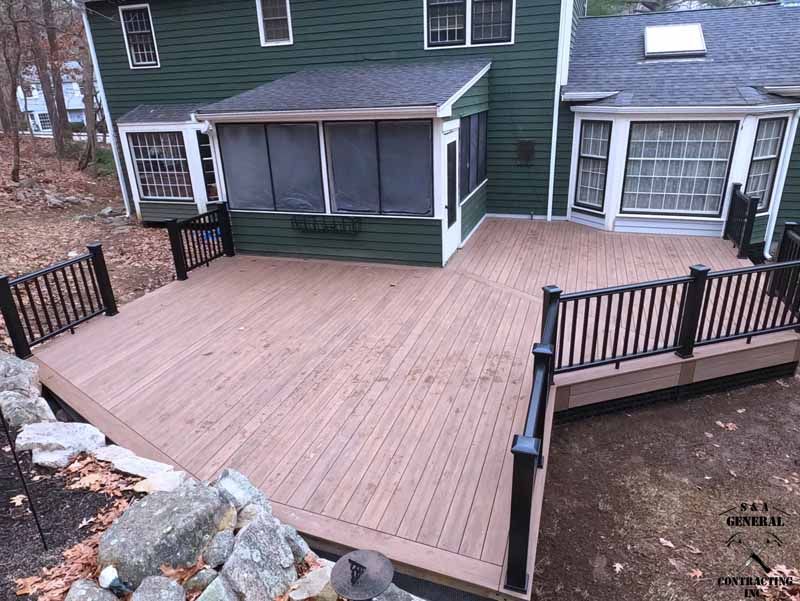 Composite deck with black railing and screened porch attached to a green house.