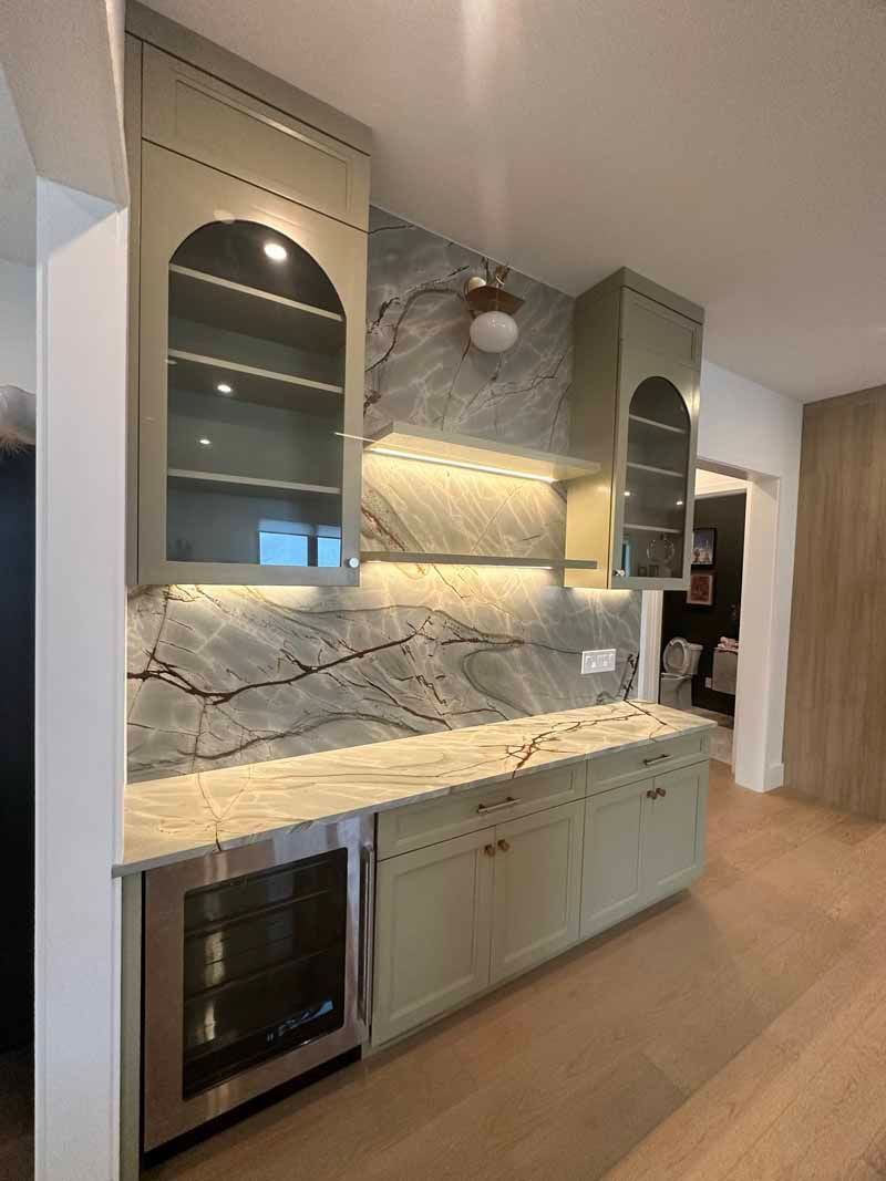 Green and marble home bar with a wine fridge, cabinets, and arched shelves.