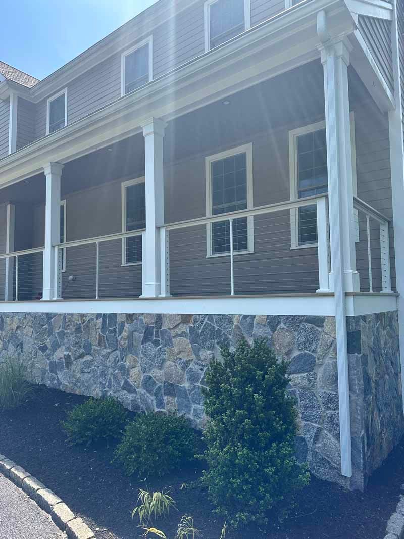 House with a stone facade base and a covered porch with glass railings and white columns.