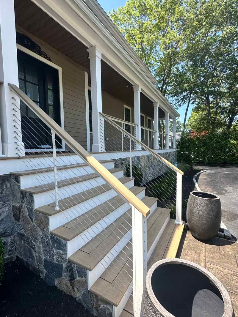 House entrance with composite stairs, cable railing, and a porch under a blue sky.